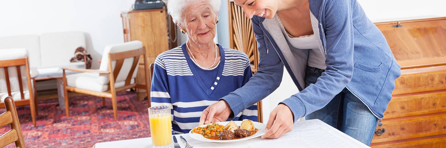 Une femme apporte un repas à une personne âgée